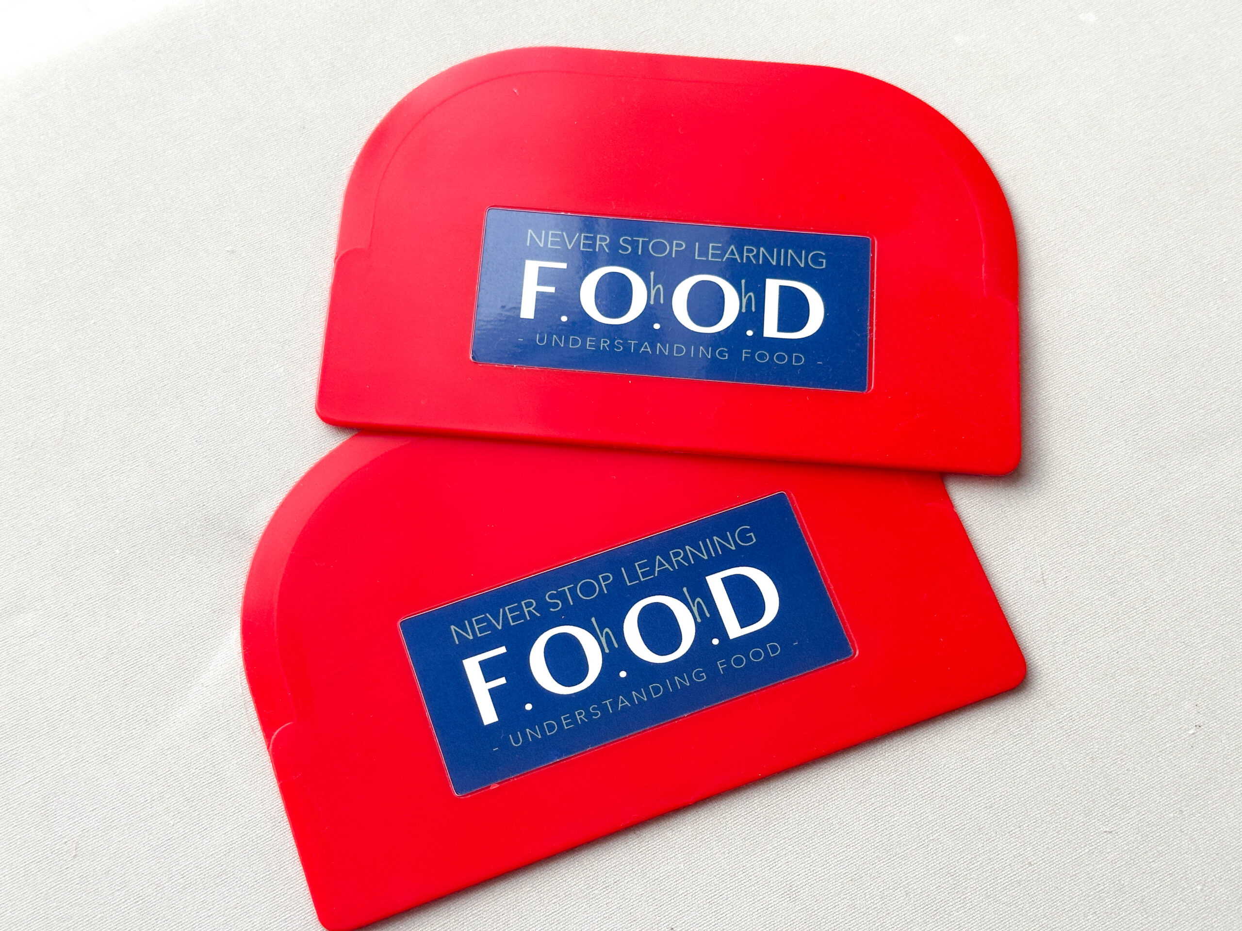 Red plastic dough scraper with dark blue F.Oh.Oh.D logo, pictured on a white background