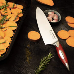 Steel chef knife with wooden handle, on a dark background amongst sliced vegetables and herbs