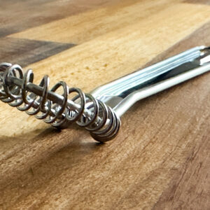 Metalic whisk with flat head for sauce making on wooden background