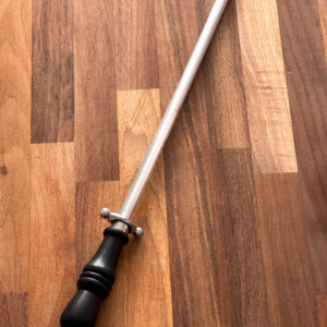 Metal honing steel for knives, with black plastic handle and silver hanging loop. Pictured against a wooden background