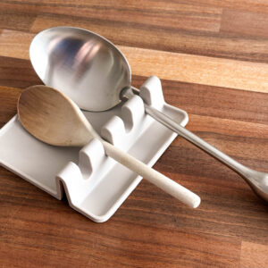 Light grey silicon spoon rest on wooden background, with wooden spoon and metal ladle