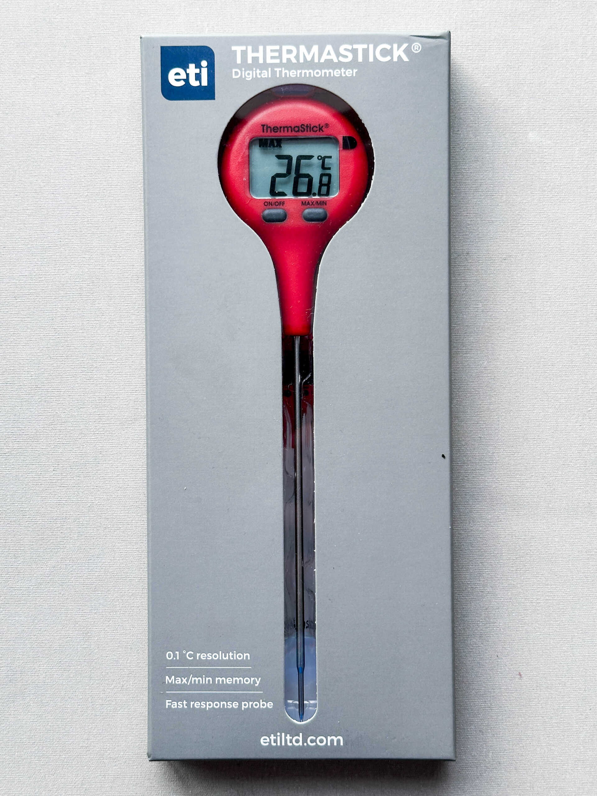 Red plastic thermometer in grey packaging on white background