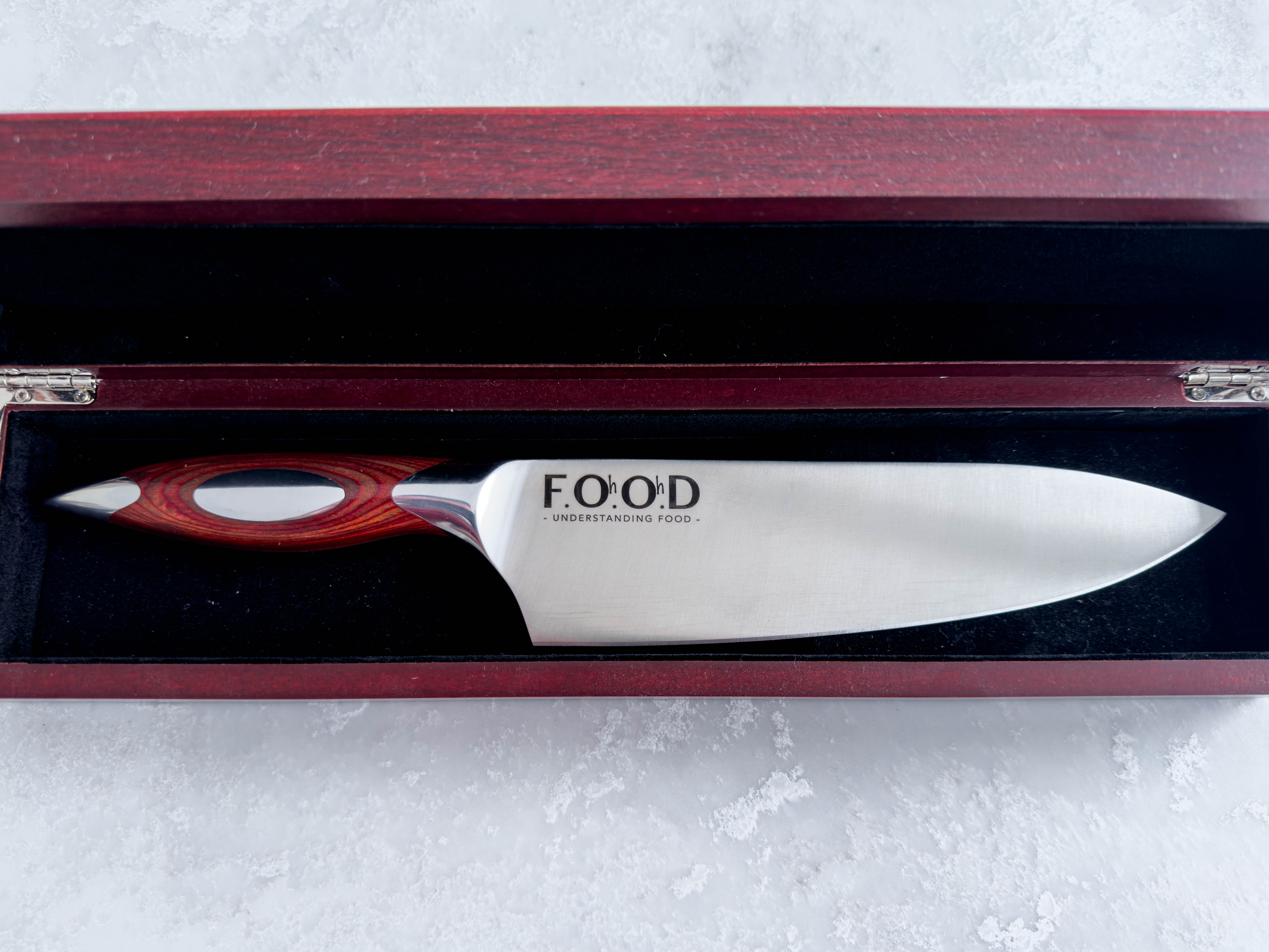 A silver metal chef knife with wooden handle, shown in a wooden presentation box against a white marbleised background