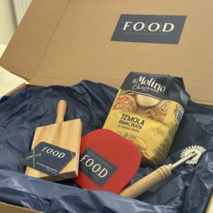 Brown cardboard gift box filled with dark blue tissue paper and pasta making tools